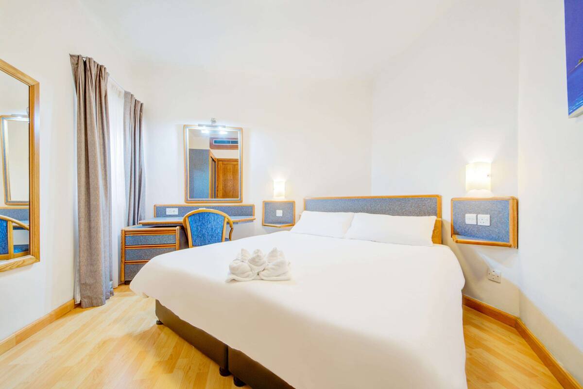 A hotel room with a large bed, a desk, a chair, a mirror, and bedside lamps.