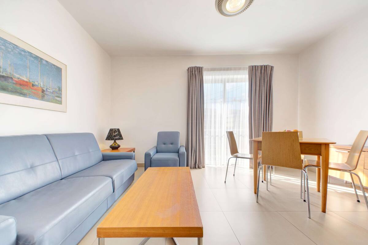 A modern living room with a sofa, a wooden table, a chair, and a dining table with chairs.