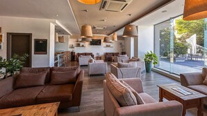 A spacious lobby with modern furniture, large windows, and a view of the outdoors. - AX Sunny Coast Resort & Spa (St. Paul's Bay)