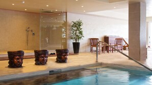 A pool area with a glass enclosure, a potted plant, and wooden chairs. - AX Sunny Coast Resort & Spa (St. Paul's Bay)
