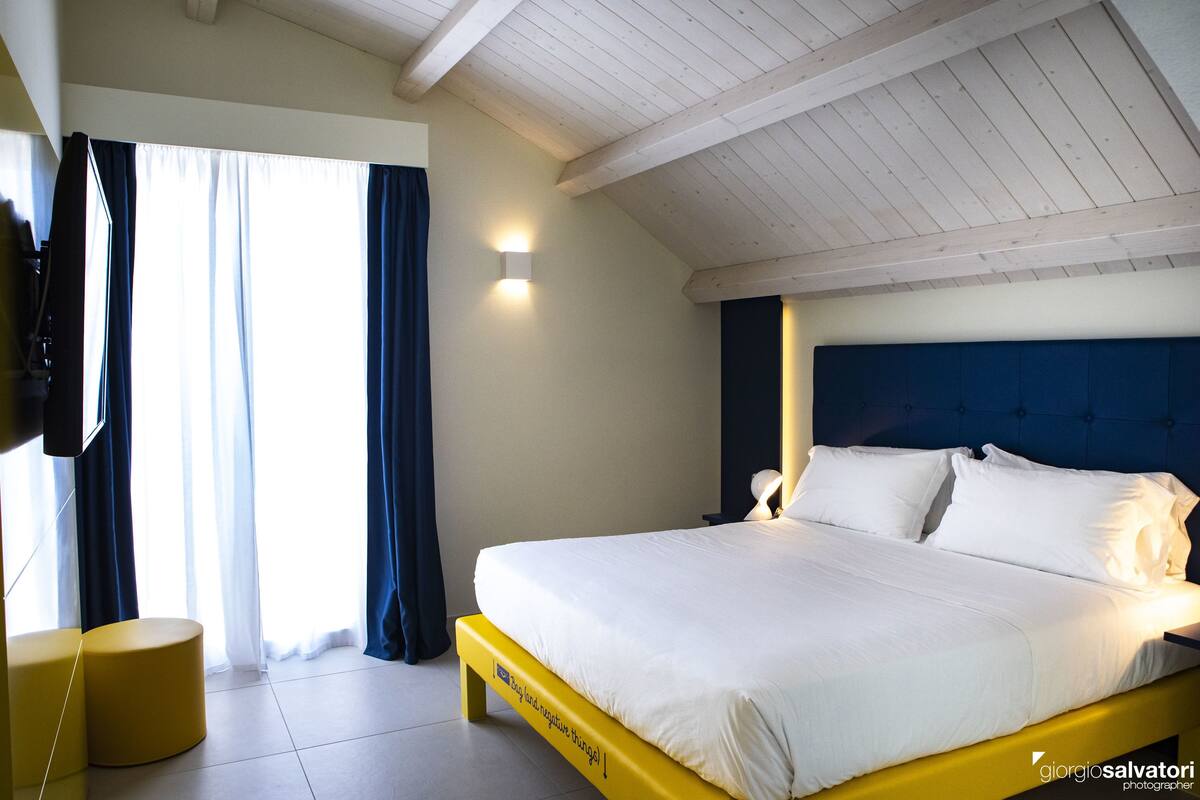 Ein modernes Hotelzimmer mit einem großen Bett, einem Flachbildfernseher und einem Fenster mit Vorhängen.