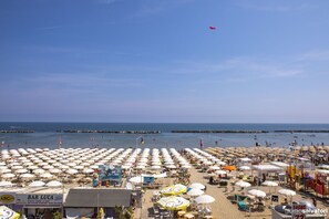 A beach with numerous umbrellas and beach chairs, a bar named 'BAR LUCA', and a view of the sea.