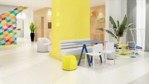 Eine moderne Hotellobby mit einer gelben Akzentwand, einer Sitzecke mit weißer und blauer Möbel und einer Treppe mit farbigem geometrischem Muster.