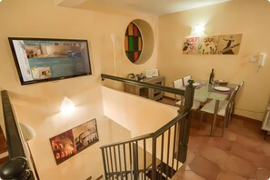 A modern interior with a flat-screen TV displaying a furniture website, a dining area with a glass table, and a staircase with a railing. - Residenza Ki - Bed & Breakfast (Rome)