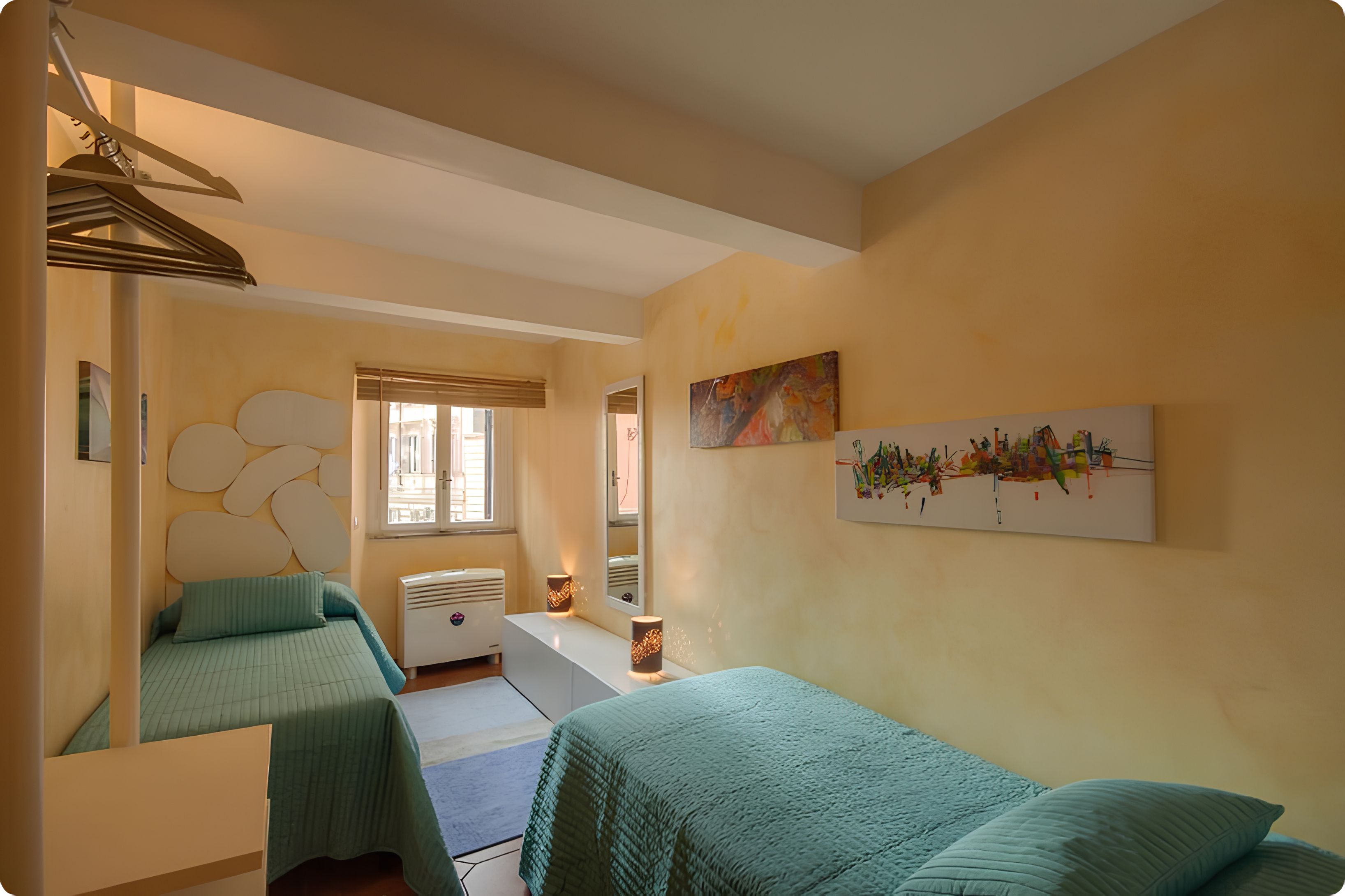 A bedroom with two beds, a window with blinds, a radiator, and wall art.