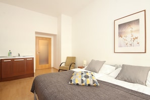 A hotel room with a bed, a chair, a desk with a lamp, and a framed picture on the wall.