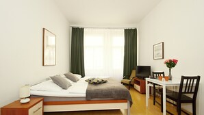 A bedroom with a bed, bedside table, lamp, TV, and a small dining area with chairs and a table. - Theatre Residence Apartments (Prague)