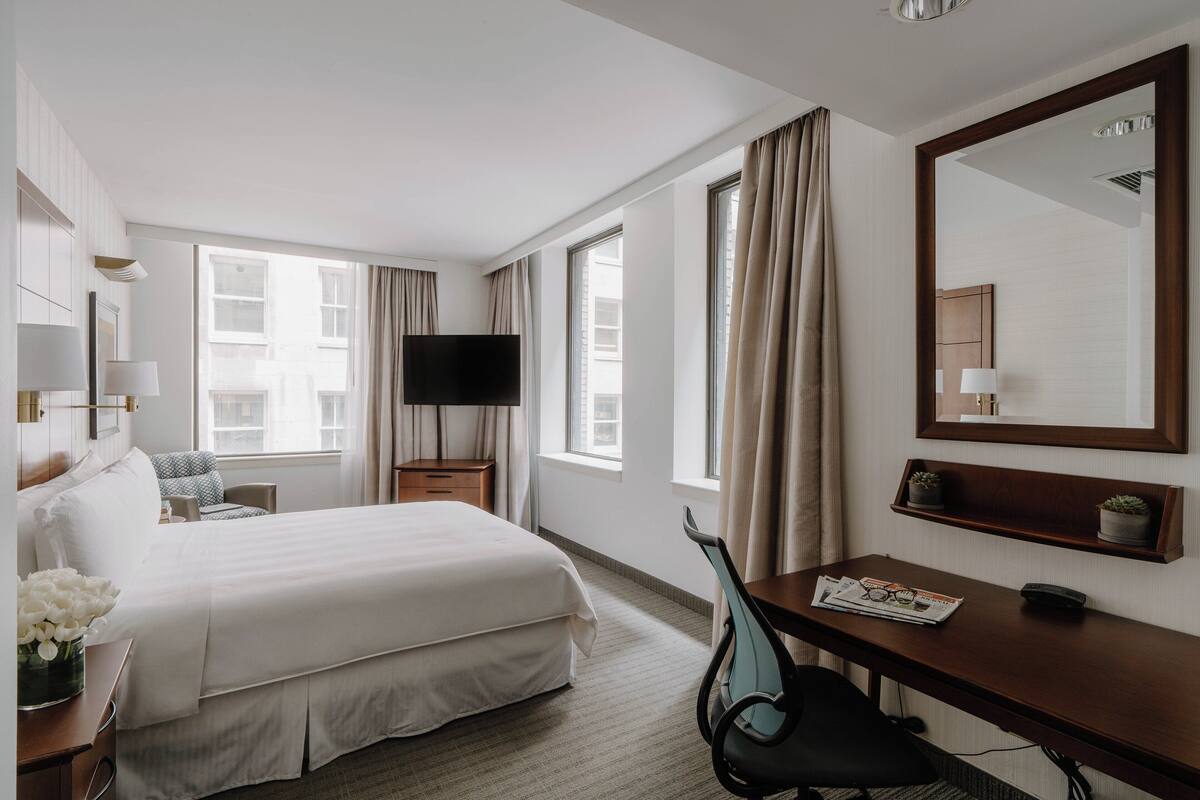 Ein Hotelzimmer mit einem großen Bett, einem Schreibtisch mit Stuhl, einem Fernseher und einem großen Spiegel.