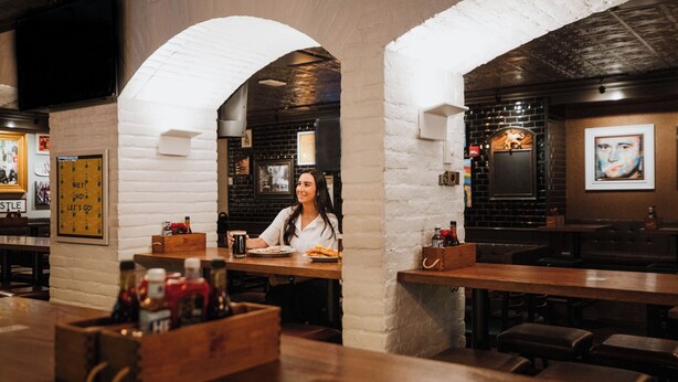 Un restaurante con paredes de ladrillo, arcos blancos y mesas de madera. Hay botellas y condimentos sobre las mesas.