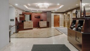 A hotel lobby with a reception desk, a chandelier, a wooden reception counter, and a sign for the Central Loop Hotel.