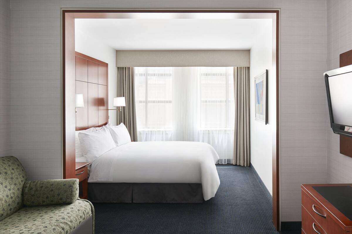 Ein Hotelzimmer mit einem großen Bett, einem Schreibtisch, einem Stuhl und einem Fernseher.
