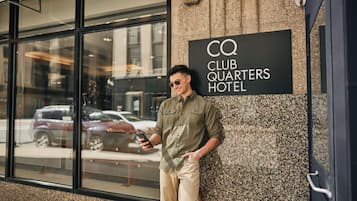 Un hombre apoyado en un edificio con un letrero que dice 'CQ Club Quarters Hotel'.