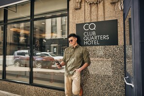 A man leaning against a building with a sign that reads "CQ Club Quarters Hotel".