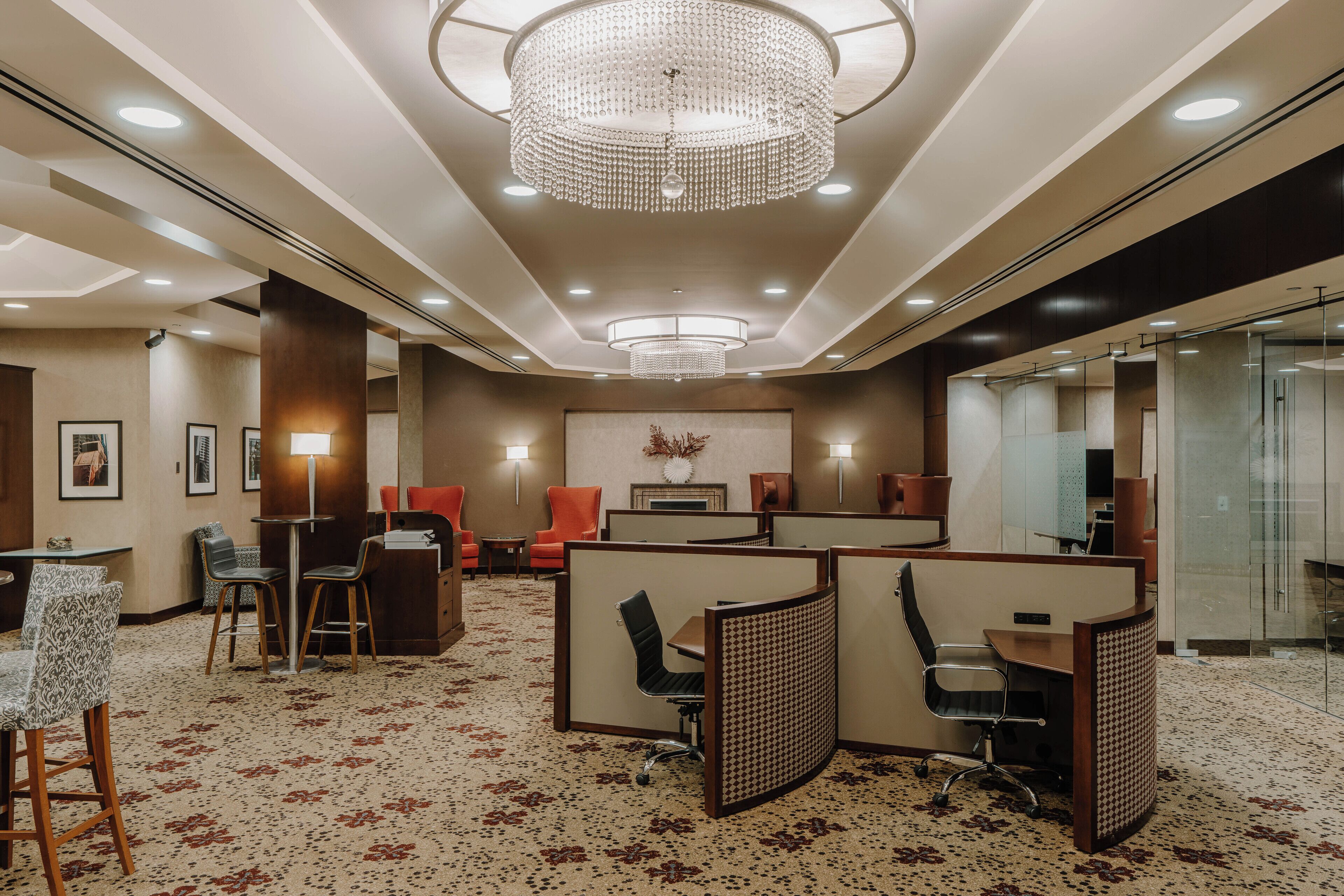 A modern hotel lobby with a central chandelier, seating areas, and a glass partition wall.