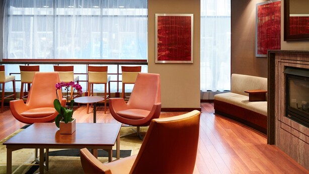 A modern lounge area with orange chairs, a sofa, and a fireplace.