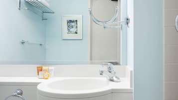 Un baño con lavamanos blanco, accesorios de cromo, un perchero, un cuadro enmarco y un espejo.