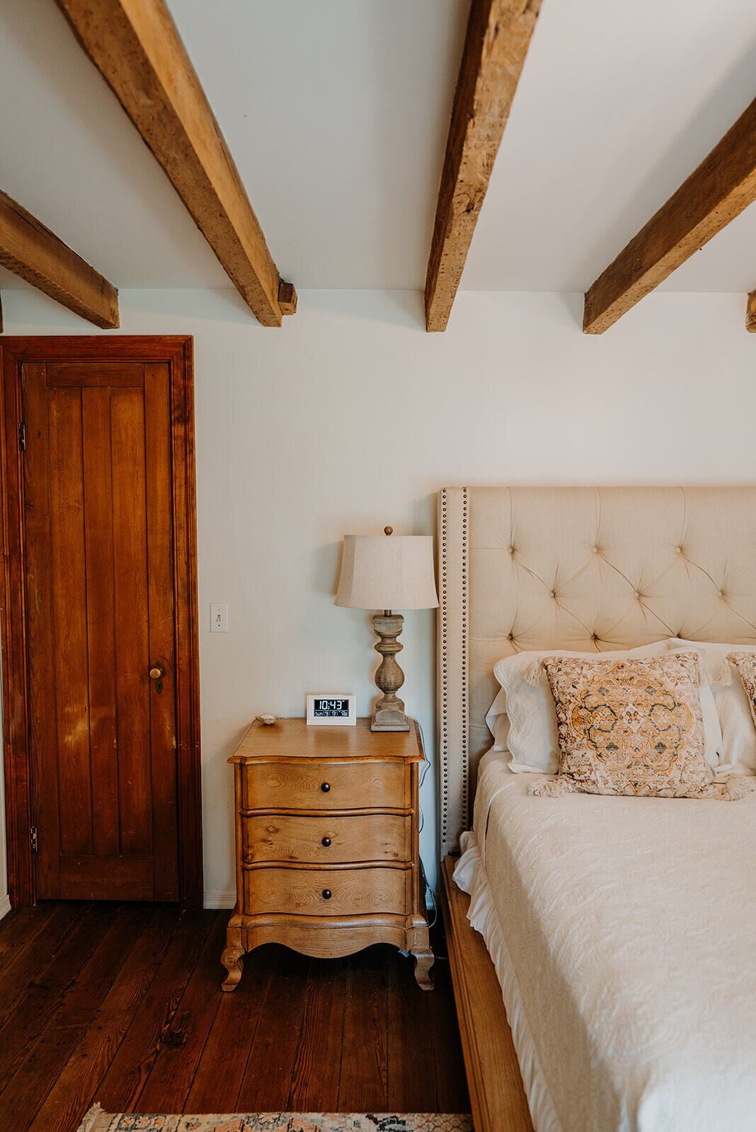 A bedroom with a wooden wardrobe, a bedside table with a lamp, and a bed with patterned pillows.