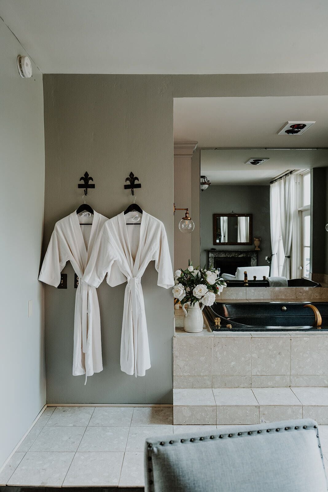 A bathroom with two white robes hanging on a wall, a sink with a vase of flowers, and a bathtub.