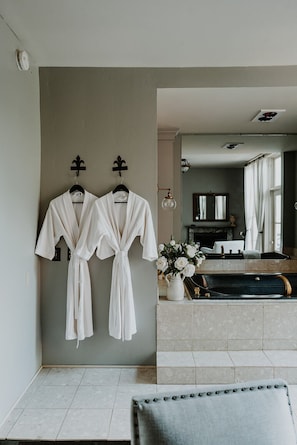 A bathroom with two white robes hanging on a wall, a sink with a vase of flowers, and a bathtub. - Mayhurst Inn (Orange)