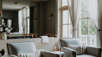 Quarto com duas poltronas, um espelho grande e uma janela com cortinas leves.