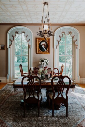 A dining room with a table set for six, surrounded by ornate chairs, a chandelier, and a framed portrait on the wall. - Mayhurst Inn (Orange)
