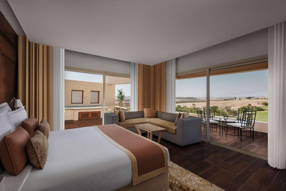 Ein Hotelzimmer mit einem großen Bett, einer Couch, einem kleinen Tisch und einem Balkon mit Blick.