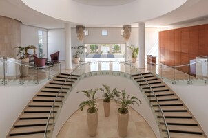 Un interior moderno con una escalera curva, barandillas de cristal y plantas en macetas.
