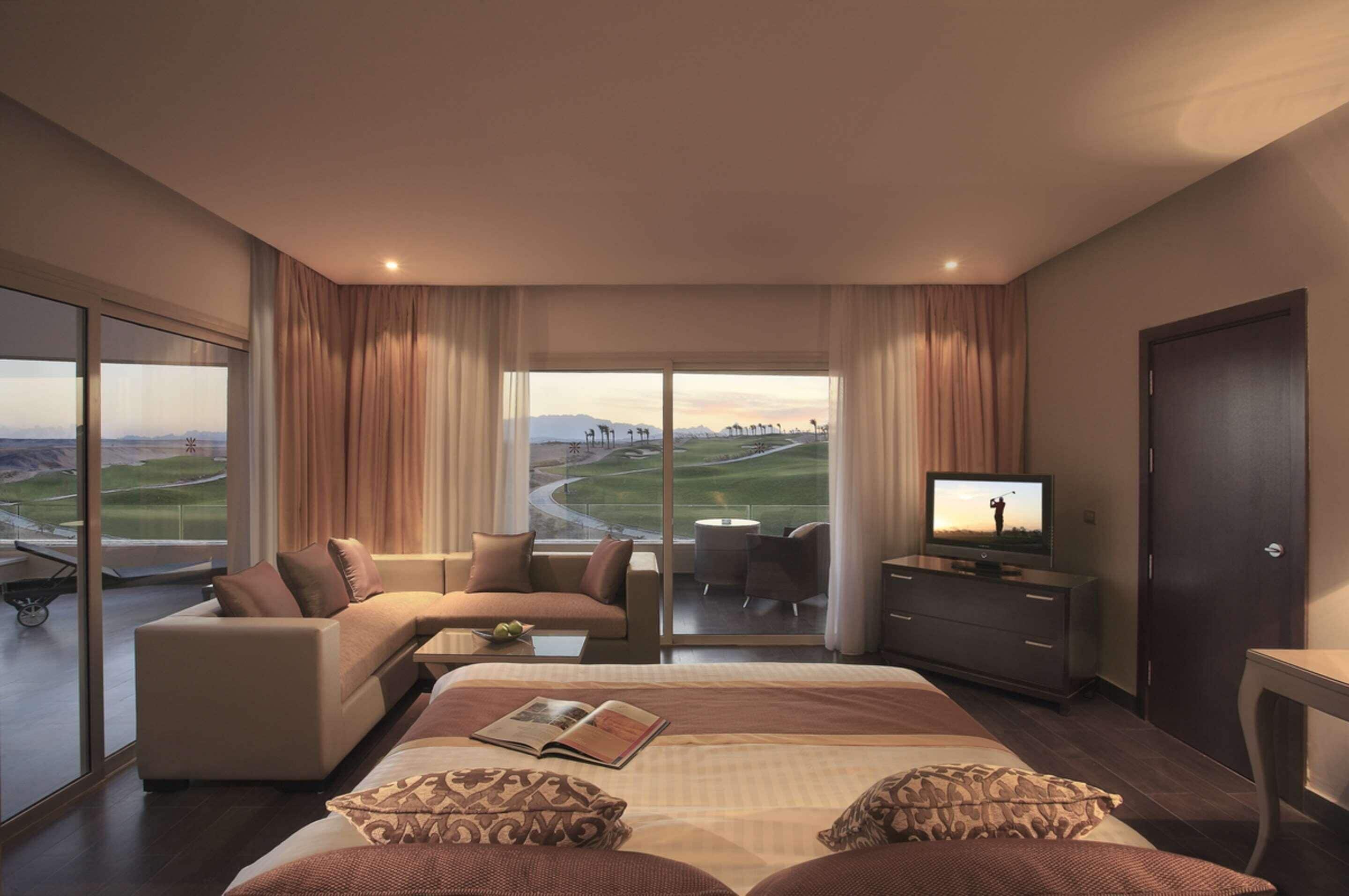 Habitación de hotel con una cama grande, un sofá, un televisor y vista a un campo de golf.