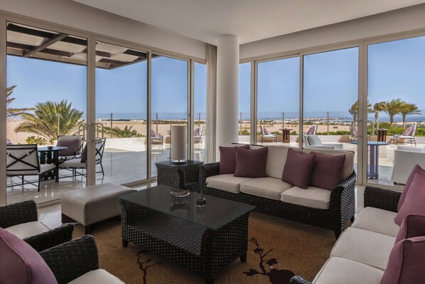 A spacious living area with a large glass door leading to a balcony with a beach view. - Steigenberger Makadi - Adults Friendly 16 Years Plus (Makadi Bay)