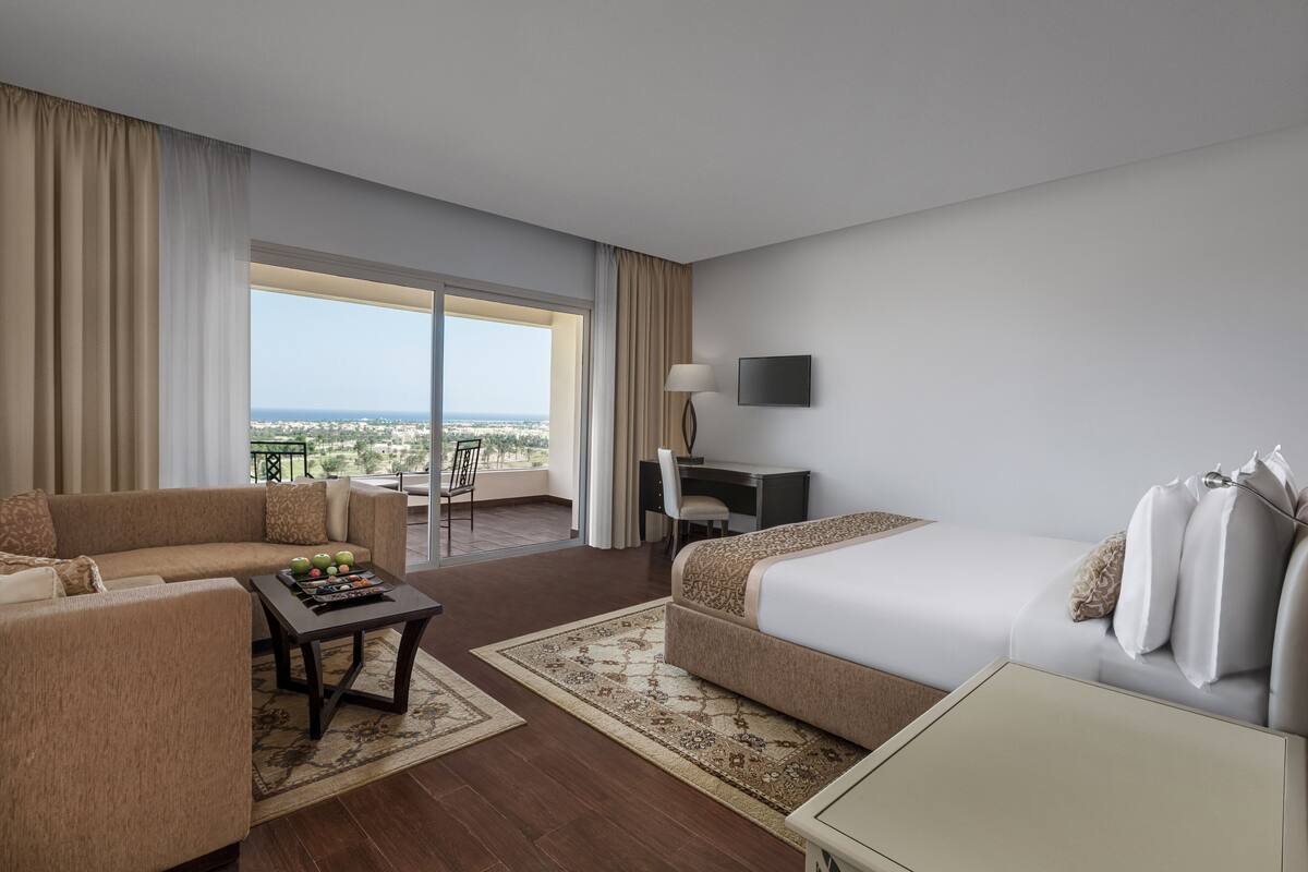 Ein Hotelzimmer mit einem großen Bett, einer Sitzecke, einem Schreibtisch und Blick auf die Stadt.