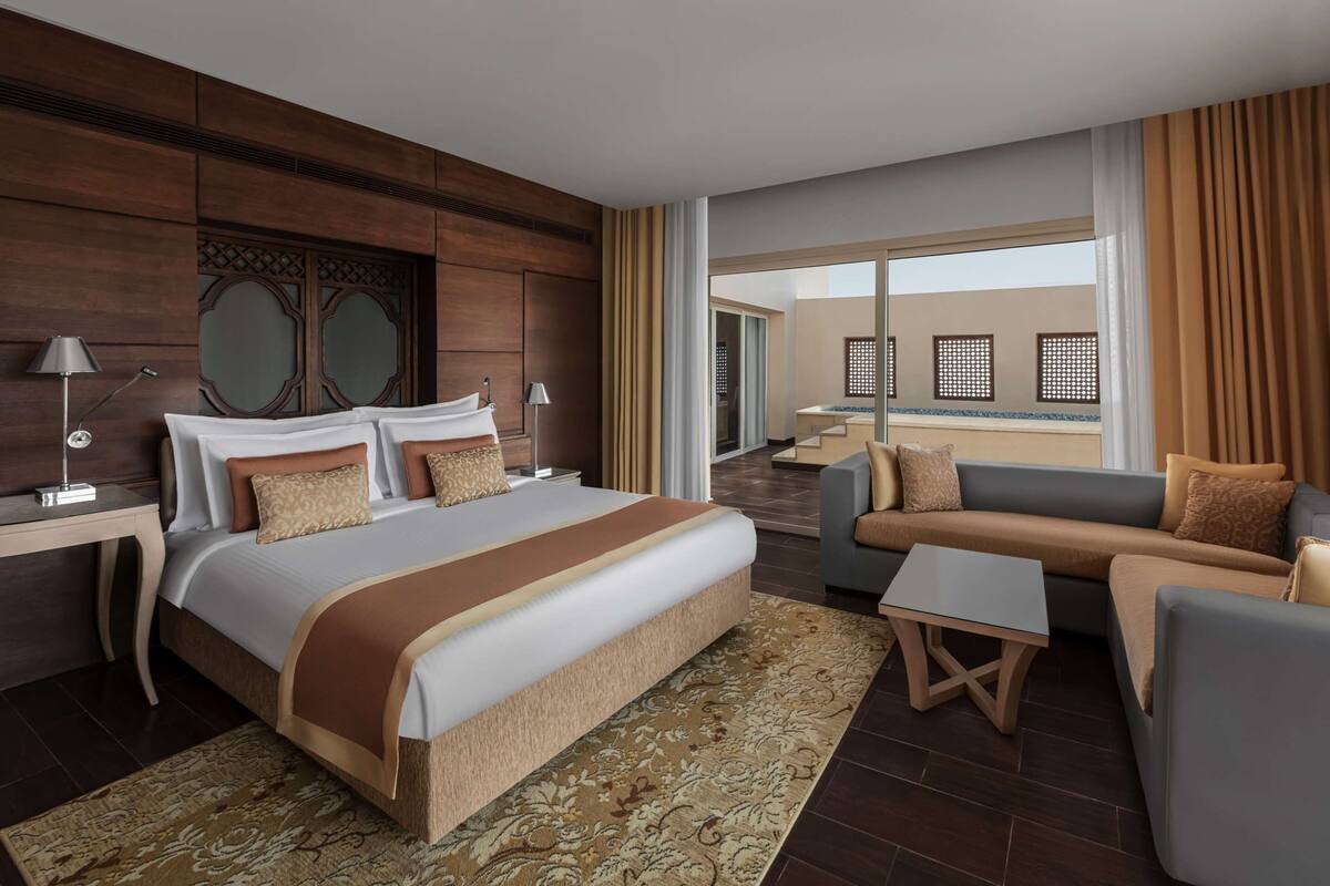 Ein Hotelzimmer mit einem großen Bett, einer Sitzecke, einem kleinen Tisch und Blick nach außen.