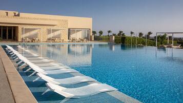 Una piscina al aire libre, sombrillas, sillones reclinables de piscina