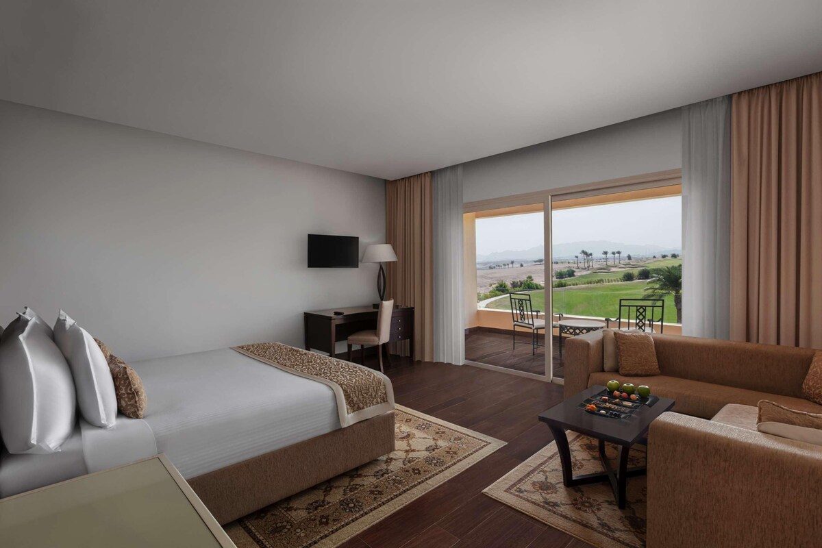 Ein Hotelzimmer mit Bett, Schreibtisch, Sofa und einem Balkon mit Blick.