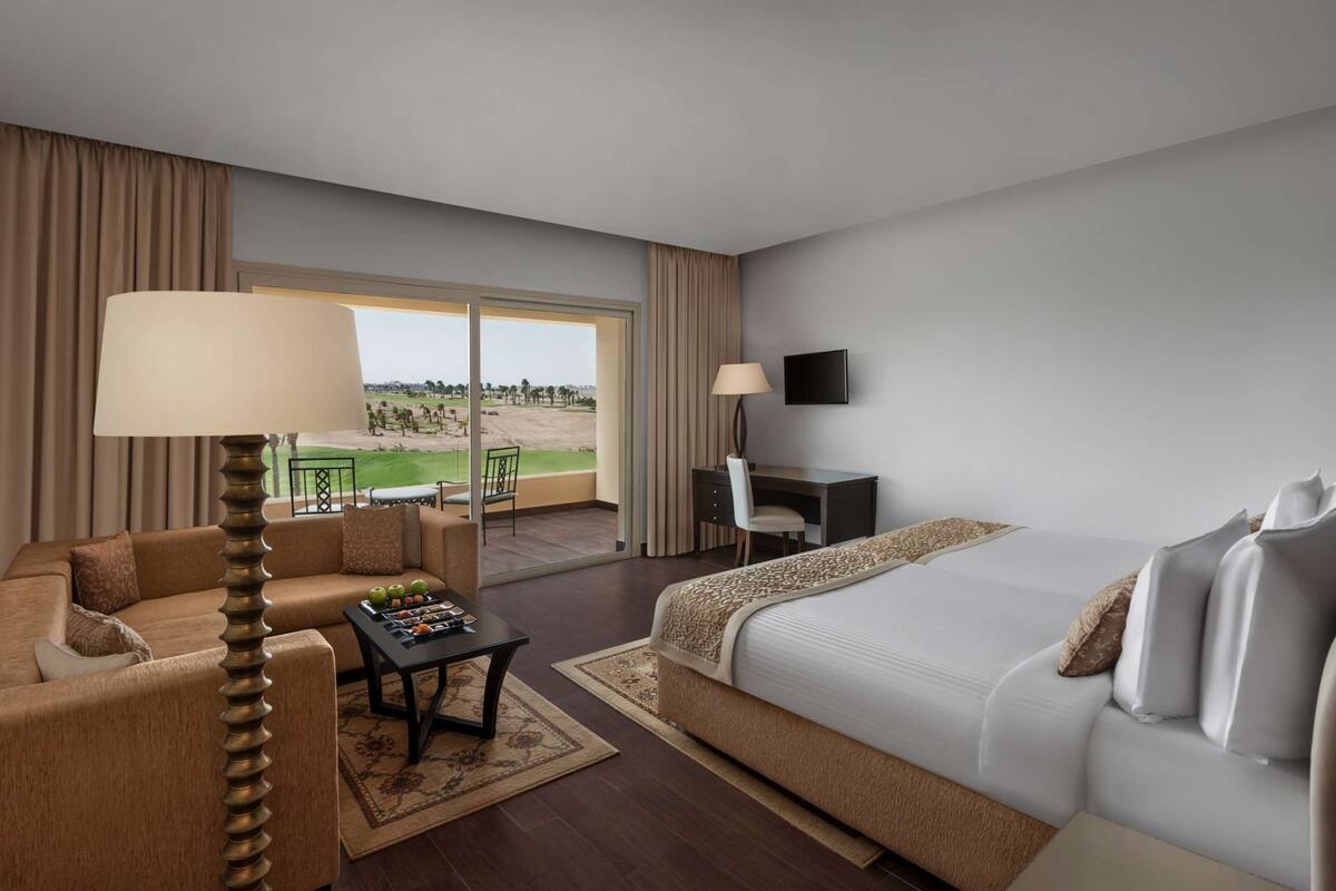 Ein Hotelzimmer mit Bett, Schreibtisch, Sessel, Sofa, Lampe und Blick auf einen Golfplatz.