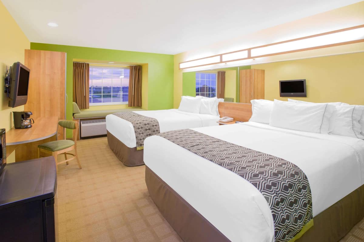 A hotel room with two beds, a desk, a chair, a TV, and a window with curtains.