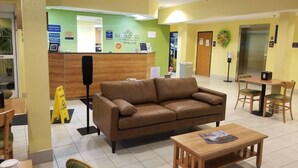 Un hall d’hôtel comprenant un comptoir d’accueil, un canapé en cuir marron, une table en bois et un coin repas avec des chaises.