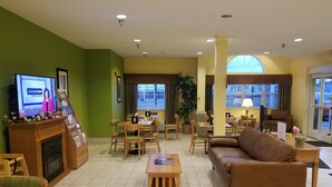 Un hall d’hôtel doté d’un téléviseur diffusant un programme d’information, d’une cheminée, d’un espace repas avec des meubles en bois et d’une grande fenêtre offrant une vue sur la ville.