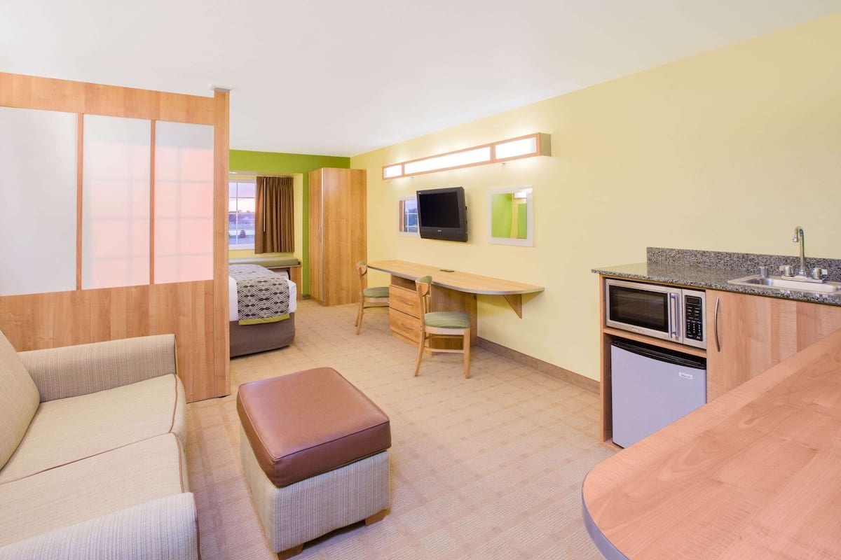 A hotel room with a bed, a desk, a kitchenette, and a seating area.