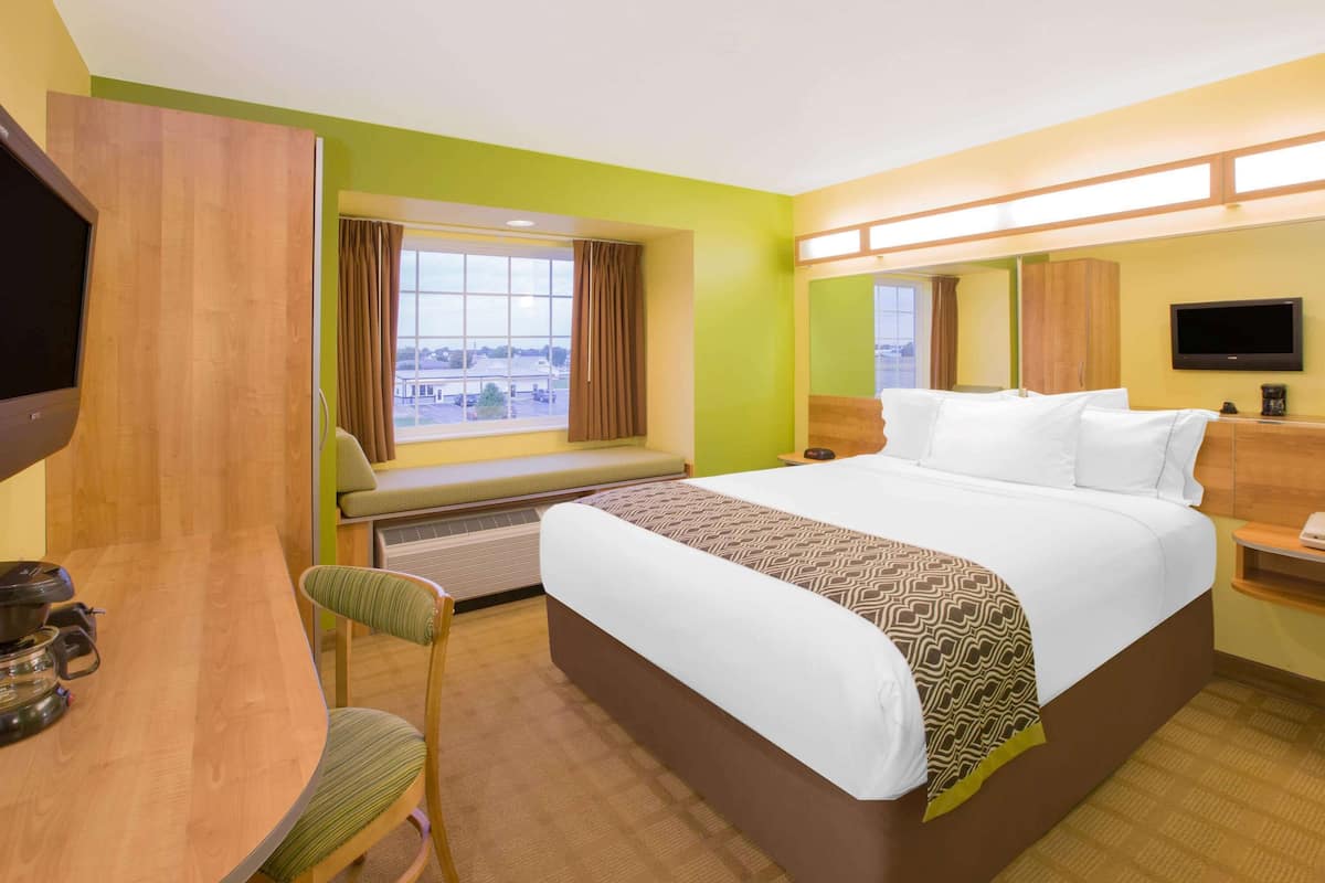 A hotel room with a large bed, a desk with a chair, a television, and a window with curtains.