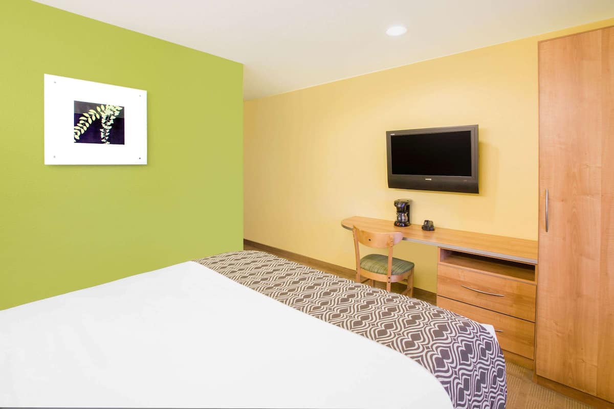 A hotel room with a bed, a desk with a chair, a television, and a wardrobe.