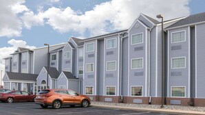 Un hôtel à plusieurs étages, avec une rangée de chambres, un parking et un ciel dégagé.