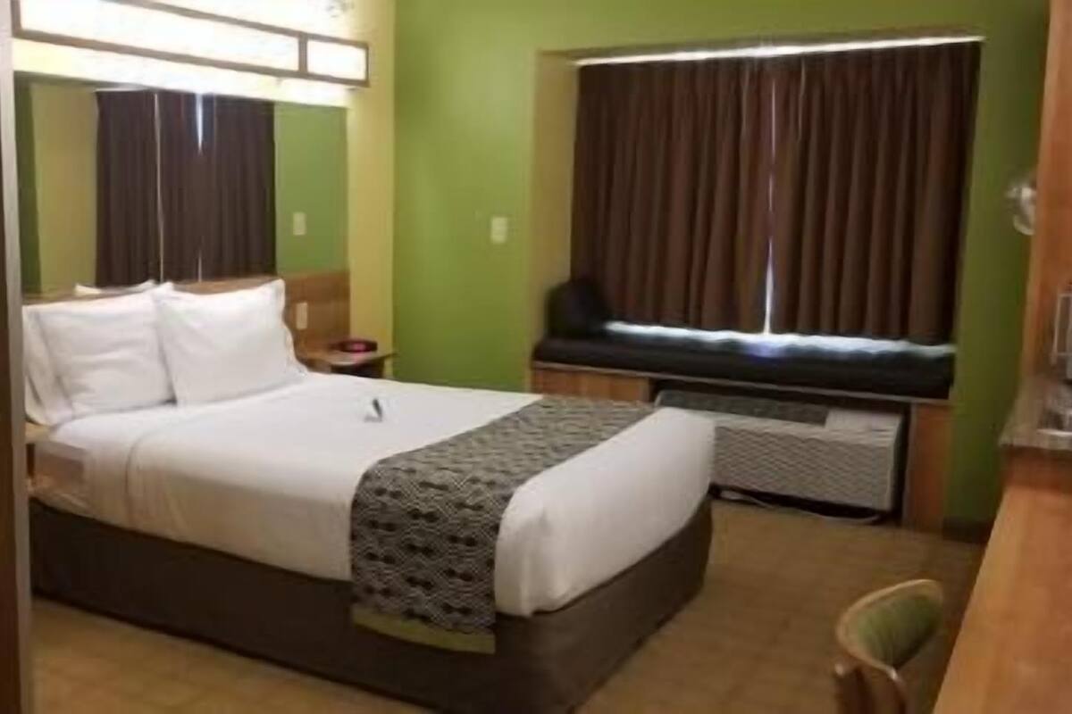 A hotel room with a bed, bedside table, and a window with curtains.