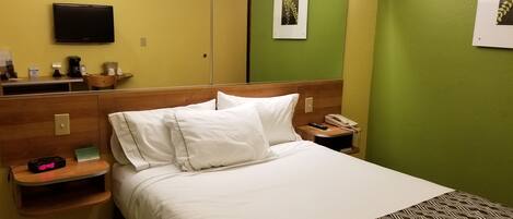 A hotel room with a bed, bedside table, alarm clock, and a telephone.