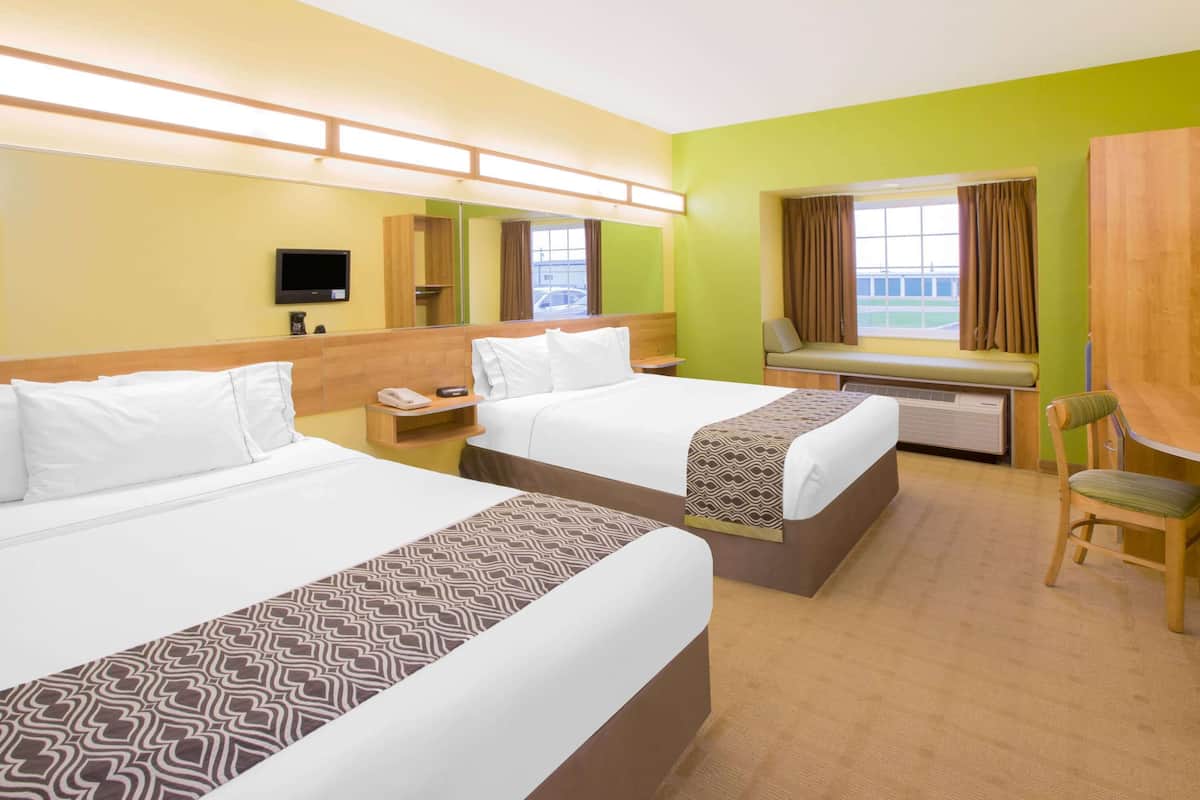 A hotel room with two beds, a desk, a chair, a TV, and a window with curtains.