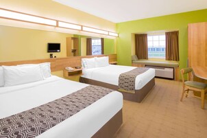 Habitación de hotel con dos camas, un escritorio, una silla, un televisor y una ventana con cortinas.