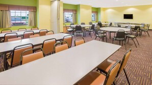 Une salle de conférence dotée de plusieurs tables et chaises, de grandes fenêtres avec des rideaux et d’un téléviseur à écran plat fixé au mur.