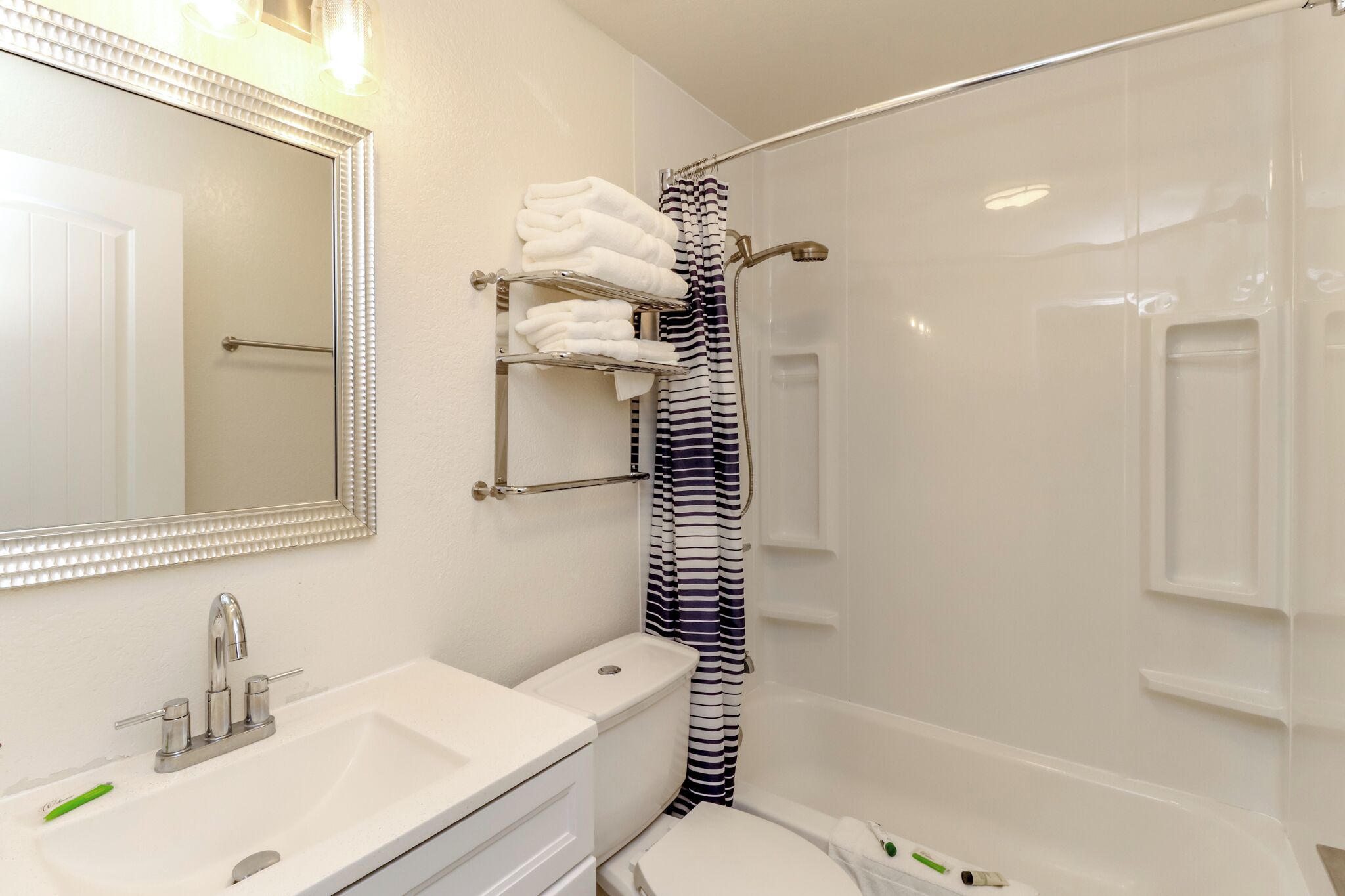 Une salle de bain avec un lavabo blanc, un miroir, des toilettes et une douche avec un rideau à rayures.