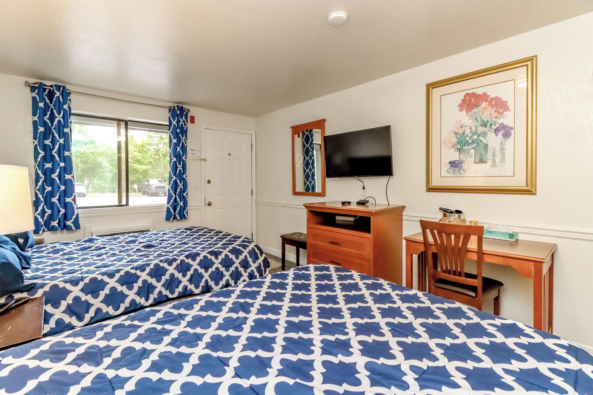 A hotel room with two beds, a desk, a chair, a TV, and a window with curtains.