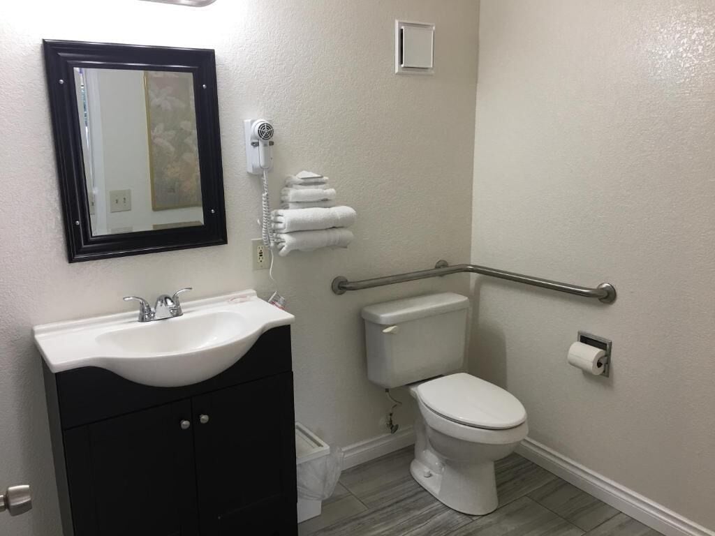 Een badkamer met een wit wastafel, toilet, handgreep en spiegel.