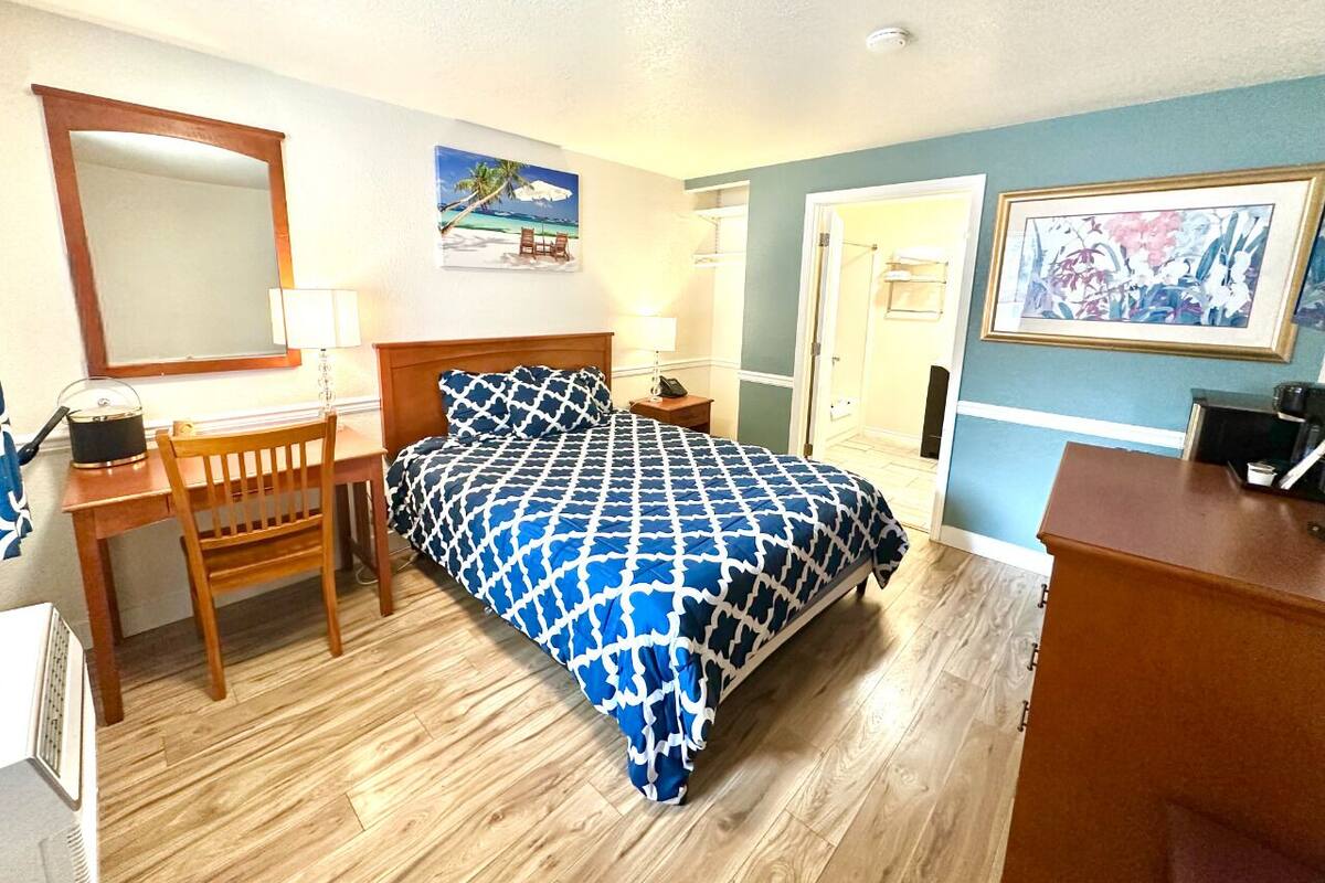A hotel room with a bed, a desk, a chair, a dresser, a mirror, and a door.